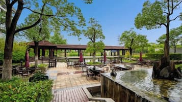 Un espace extérieur aménagé en terrasse, avec des tables et des chaises, une petite fontaine et des arbres.