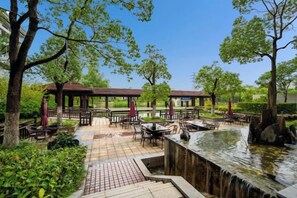 An outdoor patio area with tables and chairs, a small water feature, and trees. - Dongtai Guest House (Dongtai)