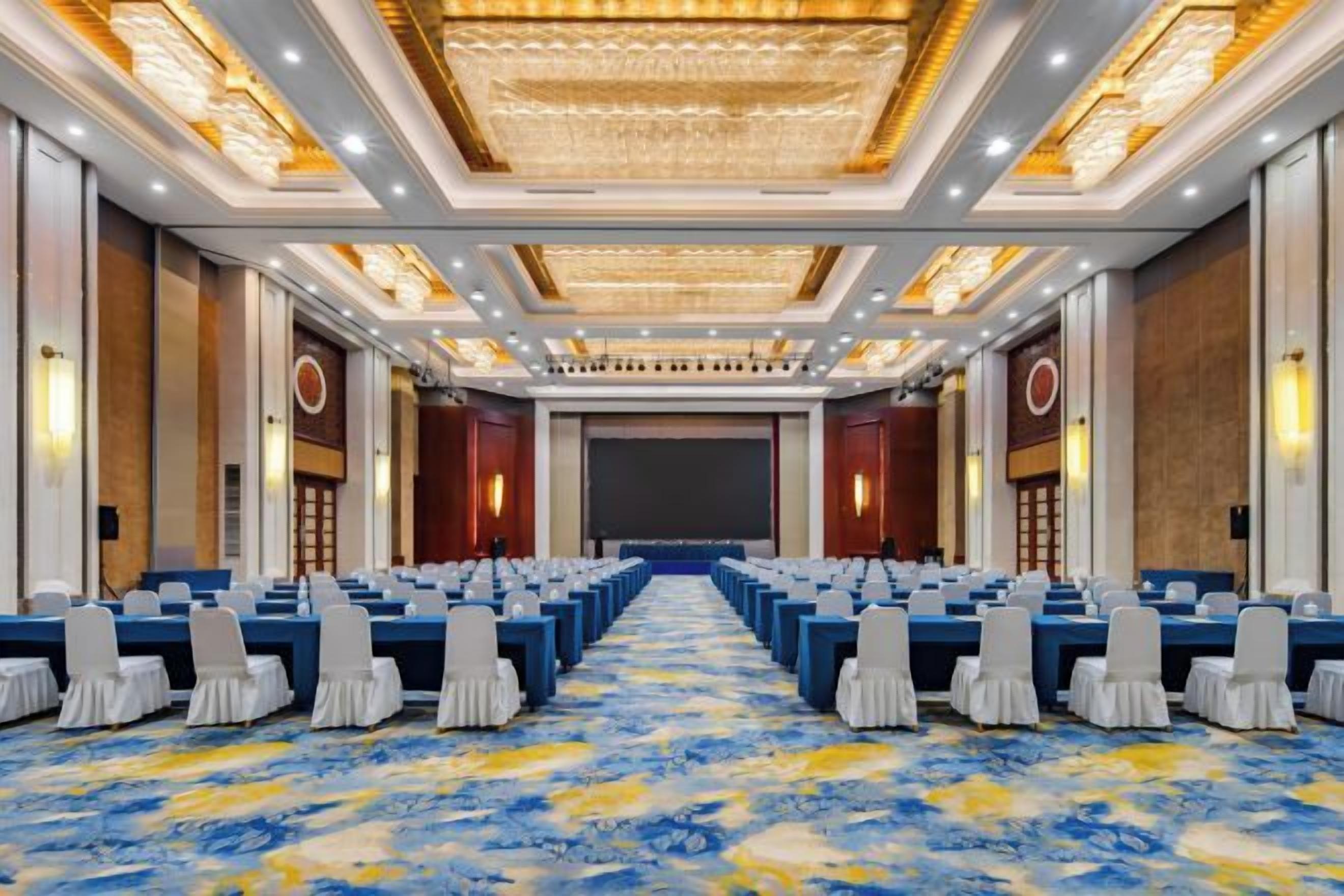 A conference room with rows of tables and chairs, a large screen, and a carpeted floor.