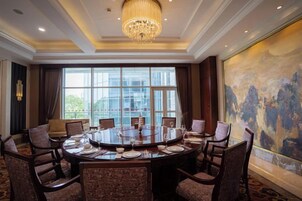 Un salón de conferencias con una mesa redonda, varias sillas y un amplio ventanal con vistas a edificios.