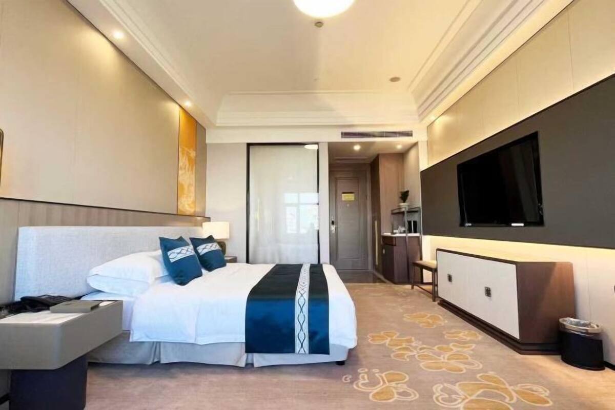 A hotel room with a bed, bedside table, TV, and a desk area.