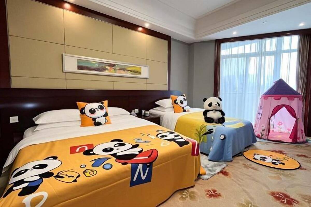 A hotel room with two beds, each with panda-themed bedding, a pink play tent, and a framed picture on the wall.