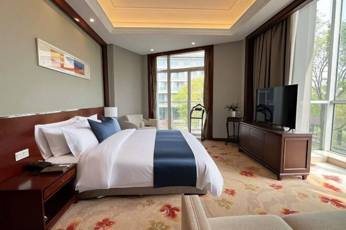 A hotel room with a bed, a TV, a dresser, and a window with a view.