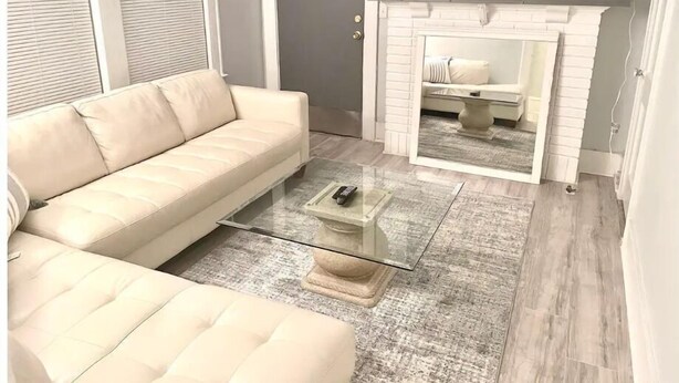 Ein Wohnzimmer mit beiger Couch, einem Glastisch, einem Kamin und einem flachbildfernseher, der darüber angebracht ist.