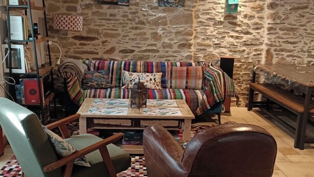 A cozy living room with a stone wall, a colorful sofa, a wooden coffee table, and a leather armchair. - Fisherman's house 50 m from the sea (Piriac-sur-Mer)