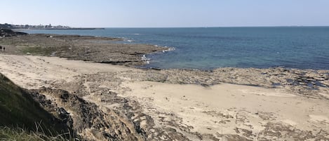 Ein felsiger Strand mit freiem Blick auf das Meer und entfernte Gebäude.
