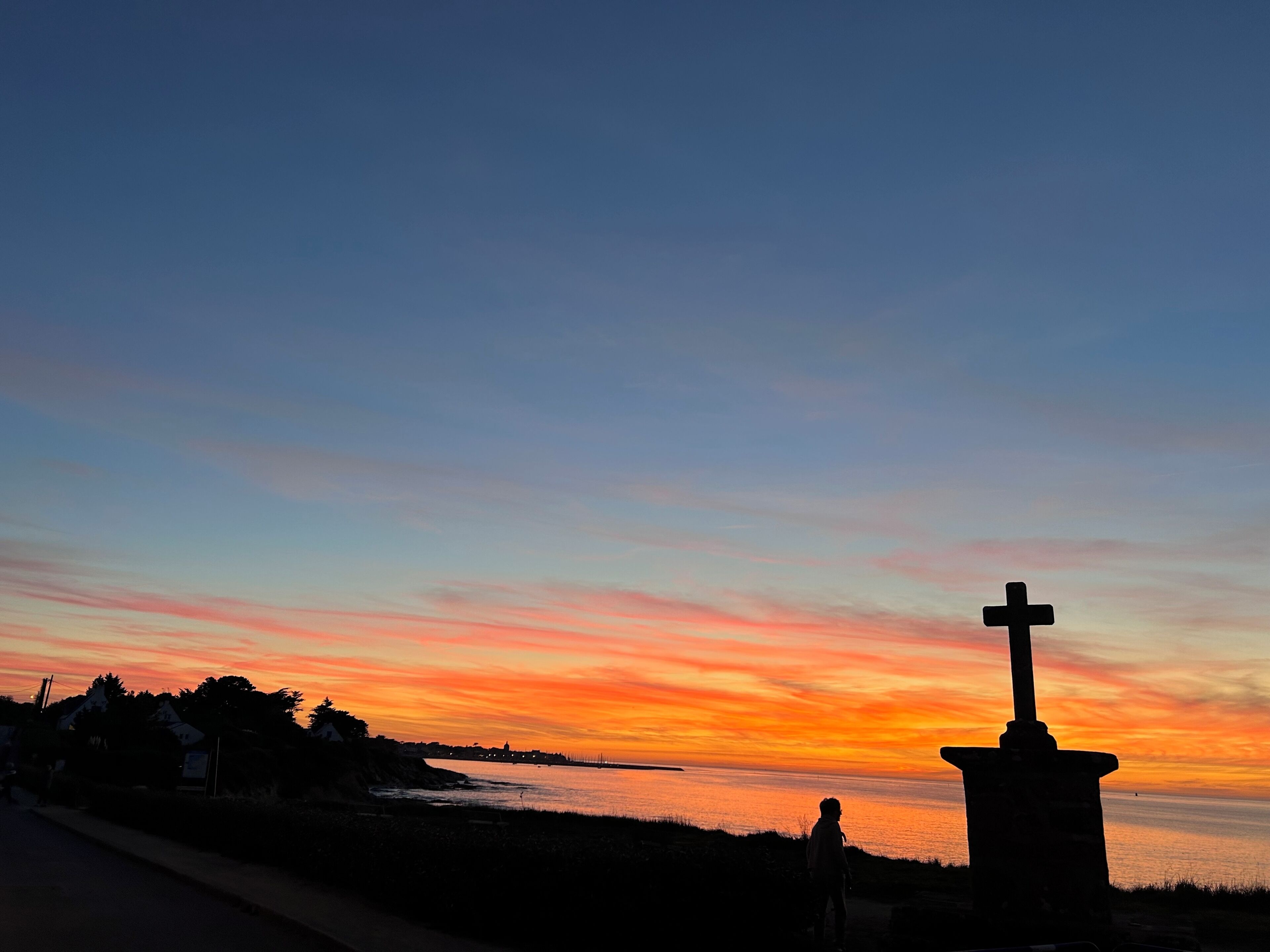 A sunset view with a cross monument on a coastal path.