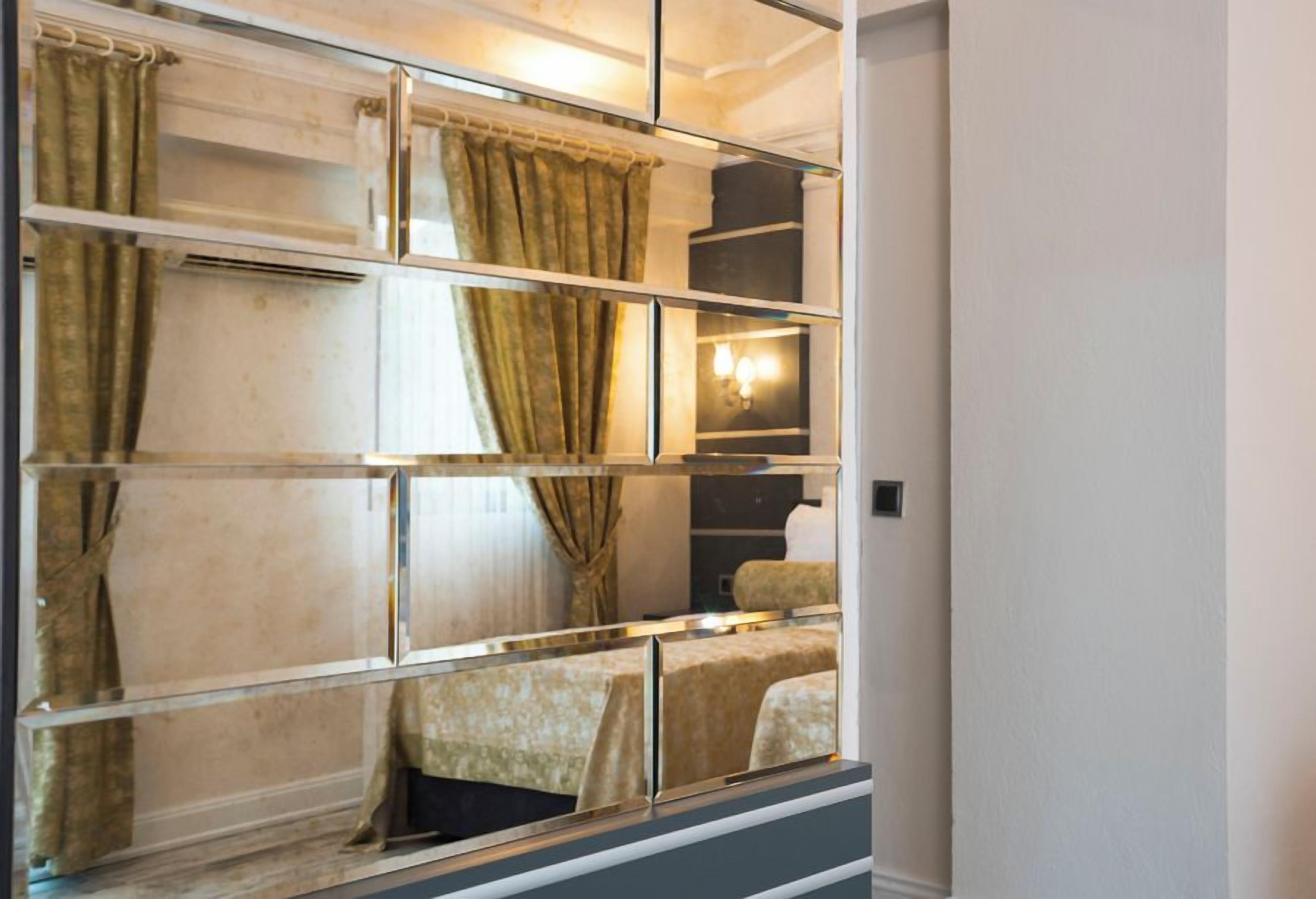A hotel room with a mirrored wall, a bed, a nightstand, and a lamp.