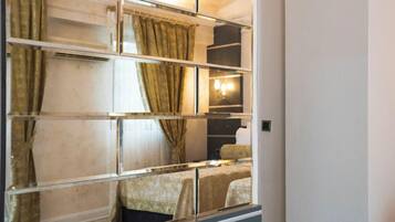 A hotel room with a mirrored wall, a bed, a nightstand, and a lamp.