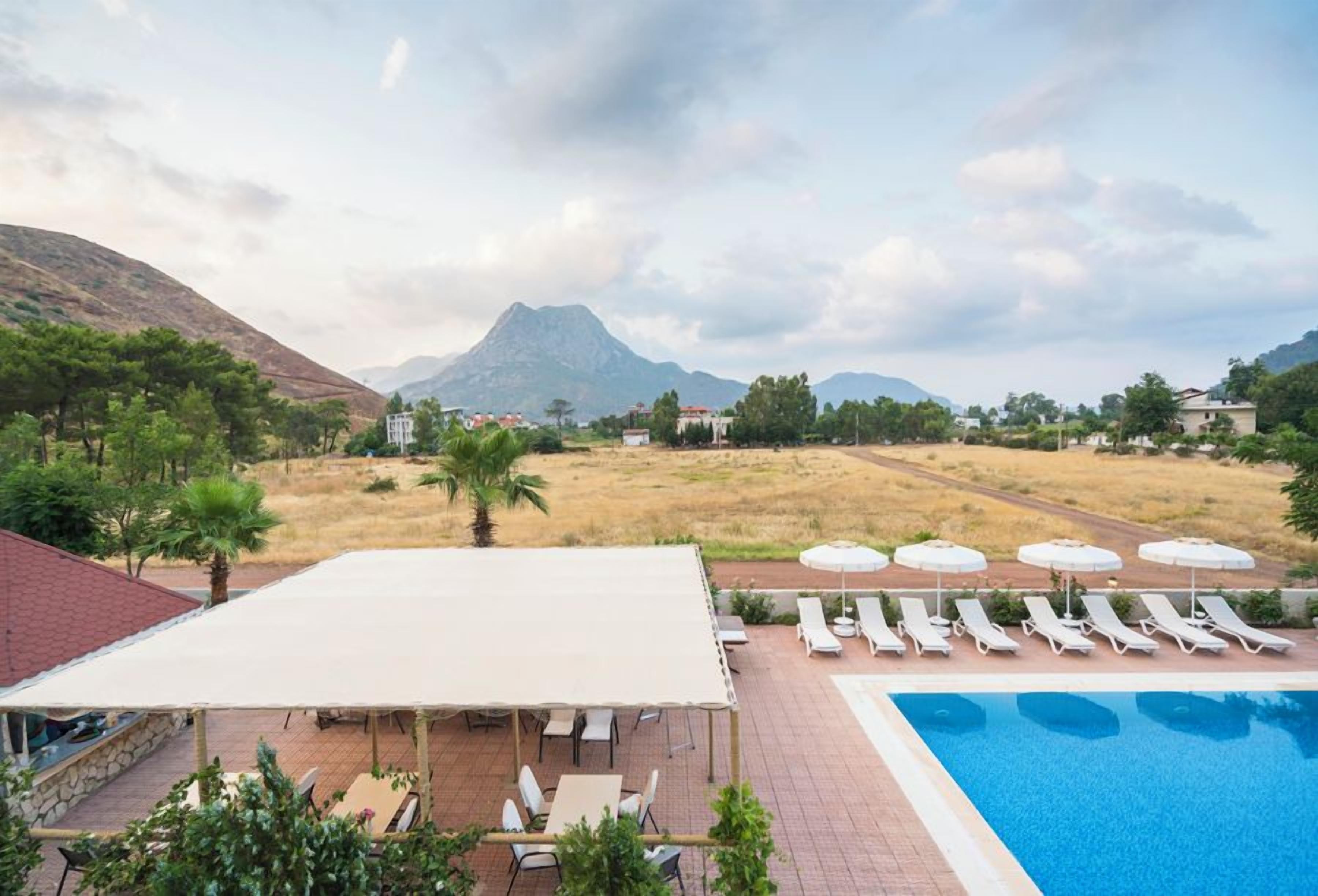 A pool area with lounge chairs and umbrellas, a covered seating area, and a mountainous backdrop.