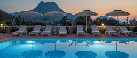 A poolside area with lounge chairs and umbrellas, a clear pool, and a mountain in the background.