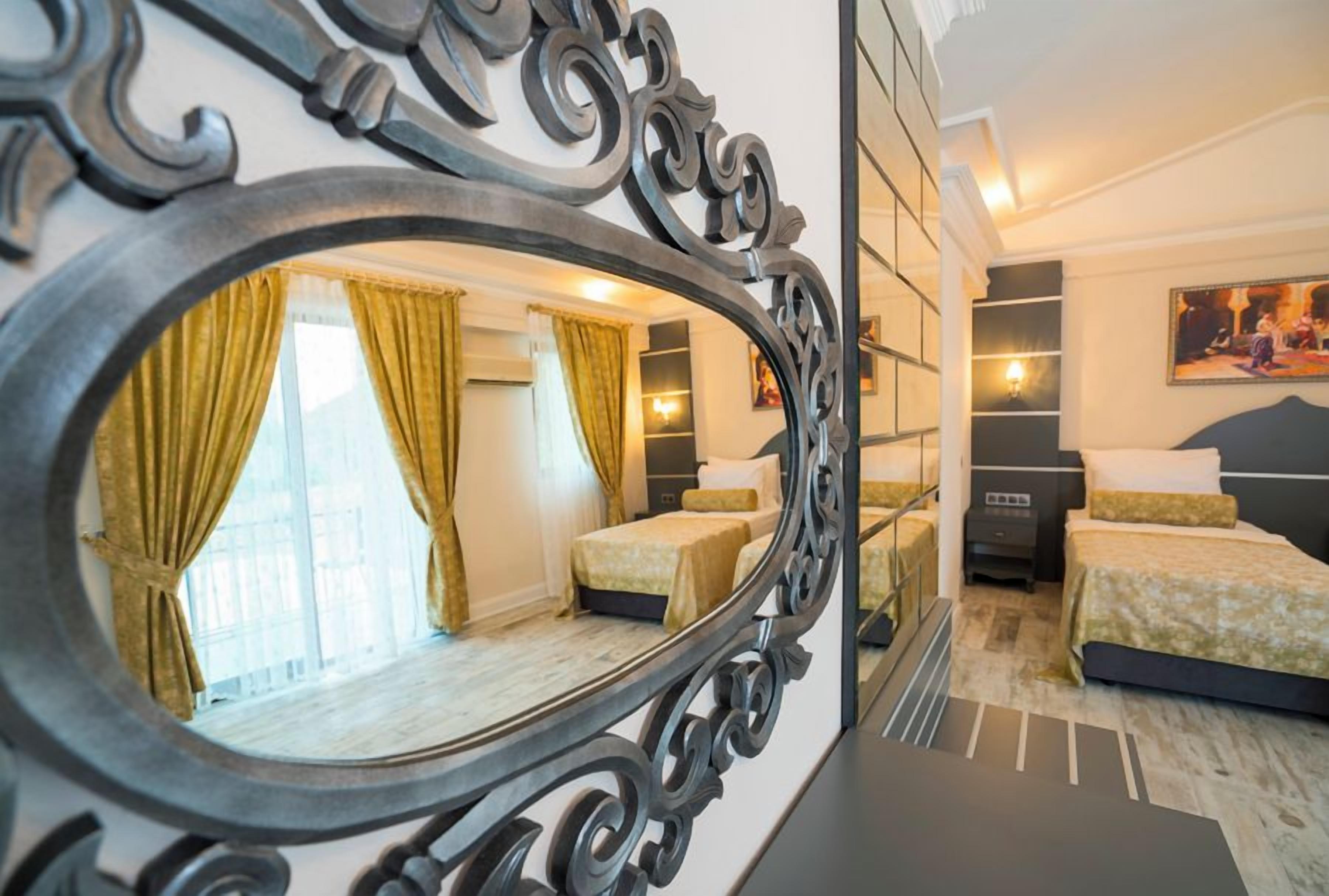 A hotel room with a large mirror, two beds, a nightstand, and a window with curtains.