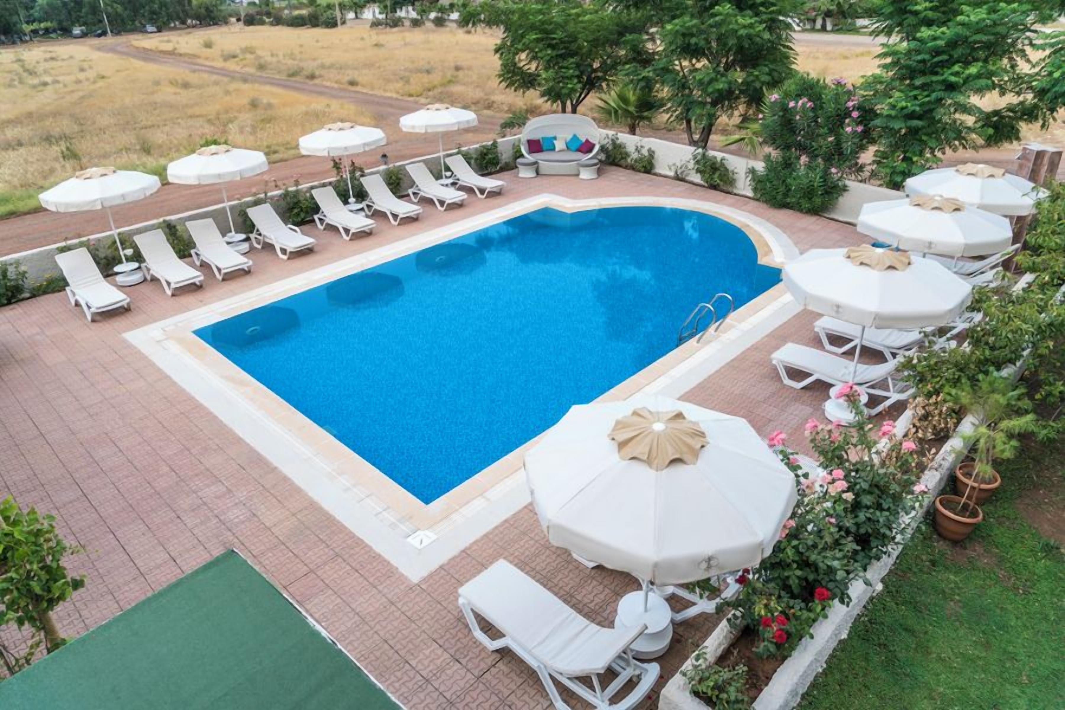 Una piscina rectangular con sillones de playa y sombrillas, rodeada de un patio de ladrillo y follaje.