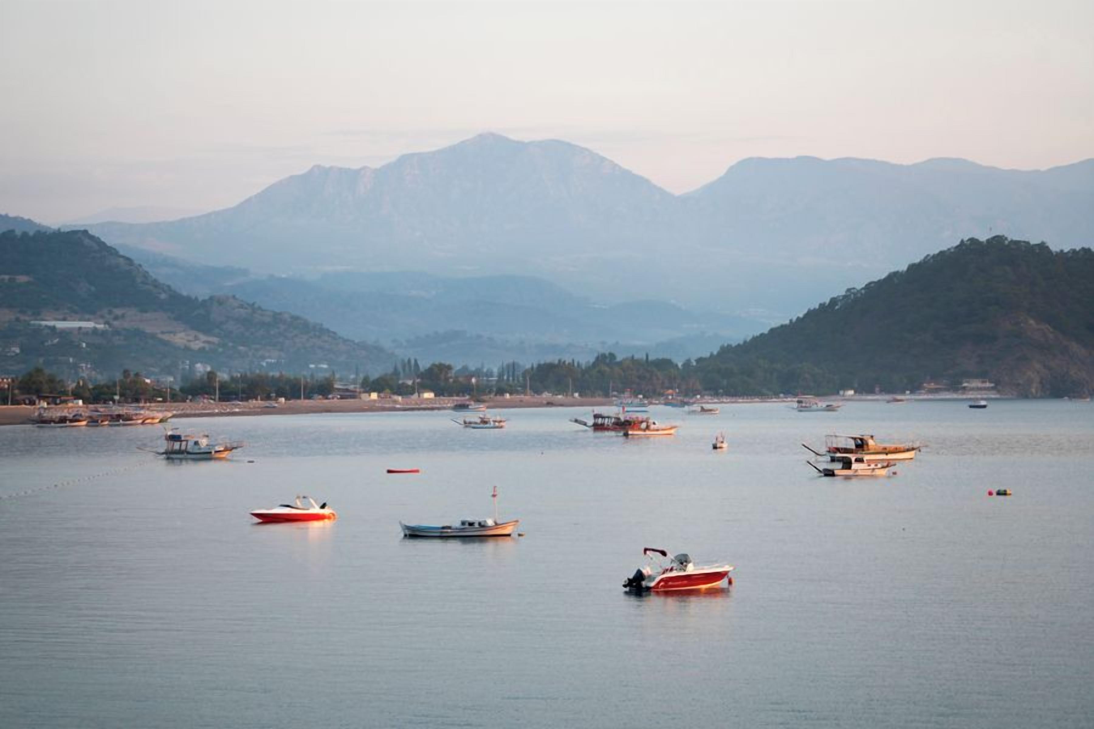Una masa de agua tranquila con varias embarcaciones, rodeada de colinas y una costa distante.