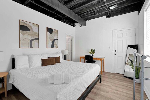 Une chambre à coucher moderne avec un grand lit, un bureau et deux tableaux abstraits accrochés au mur.