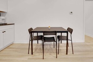 A dining area with a table and four chairs, a coffee maker on the counter, and a thermostat on the wall.