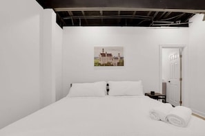 A white room with a bed, a painting of a castle, and a door.