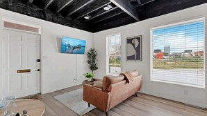 Een moderne woonkamer met een bank, een schilderij en een raam met zonwering.