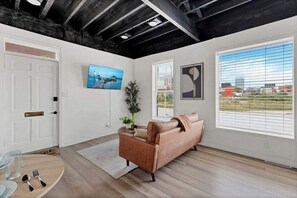 A modern living room with a sofa, a painting, and a window with blinds.