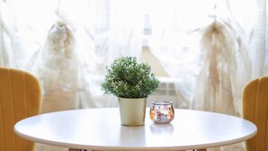 A round table with a white top and wooden legs, flanked by two yellow chairs with wooden frames. A small potted plant and a decorative candle holder are placed on the table. - confortable accomodation in a safe area (București)