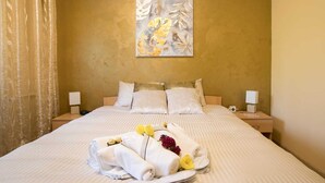 A hotel room with a large bed, two bedside tables, a wall-mounted painting, and a neatly made bed with towels and flowers. - confortable accomodation in a safe area (București)