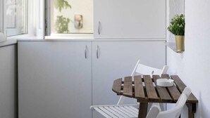 A small, enclosed balcony with a white cabinet, a wooden table, and two white chairs. - confortable accomodation in a safe area (București)
