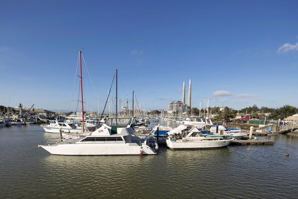 A marina with several boats docked, a clear sky, and industrial buildings in the background.