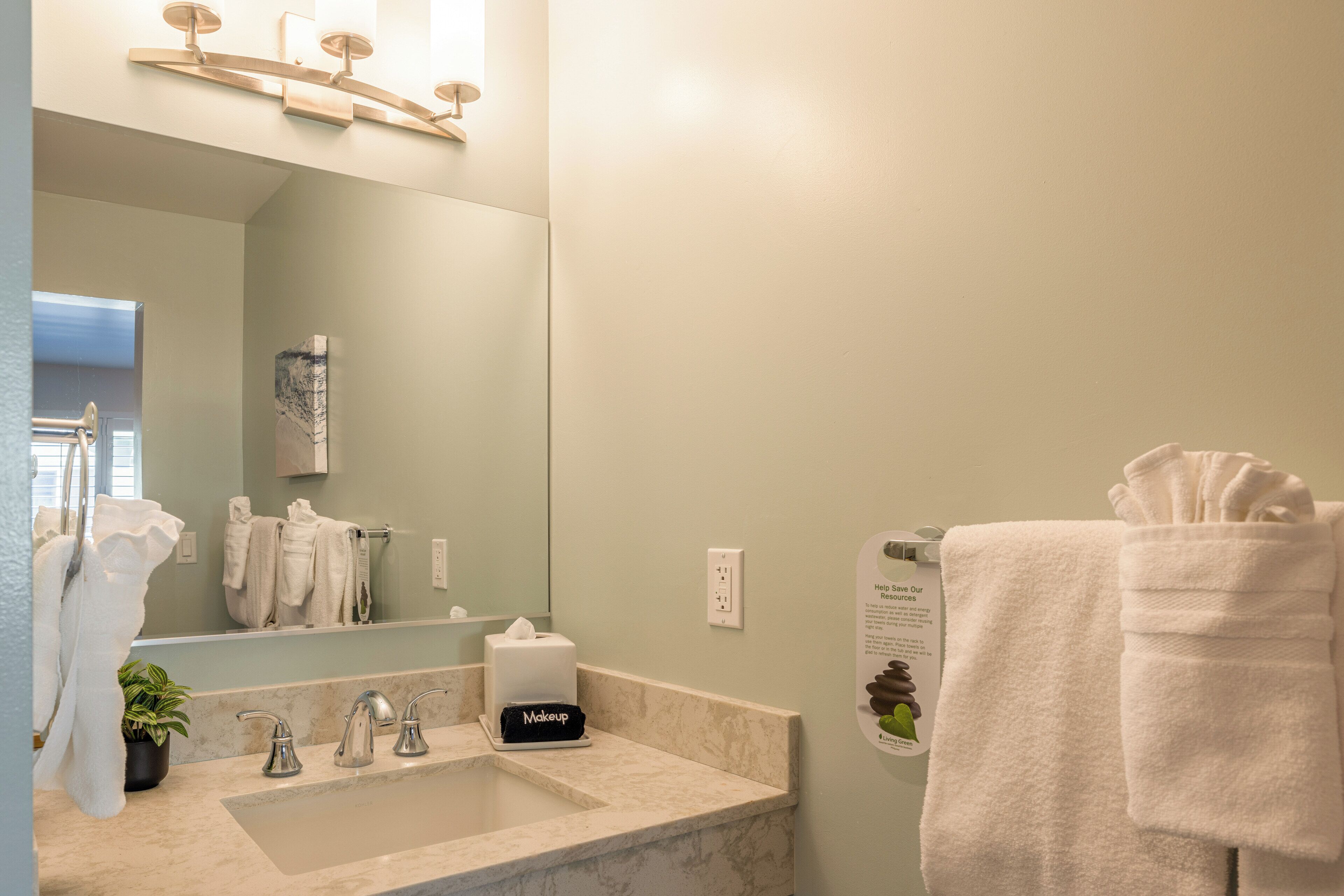 A bathroom with a sink, mirror, towel rack, and a makeup station.