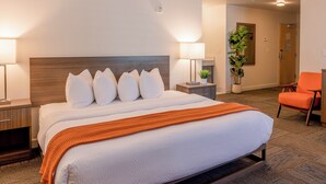 A hotel room with a large bed, two bedside tables, a nightstand, a chair, and a potted plant. - Inn At Moss Landing Point (Moss Landing)
