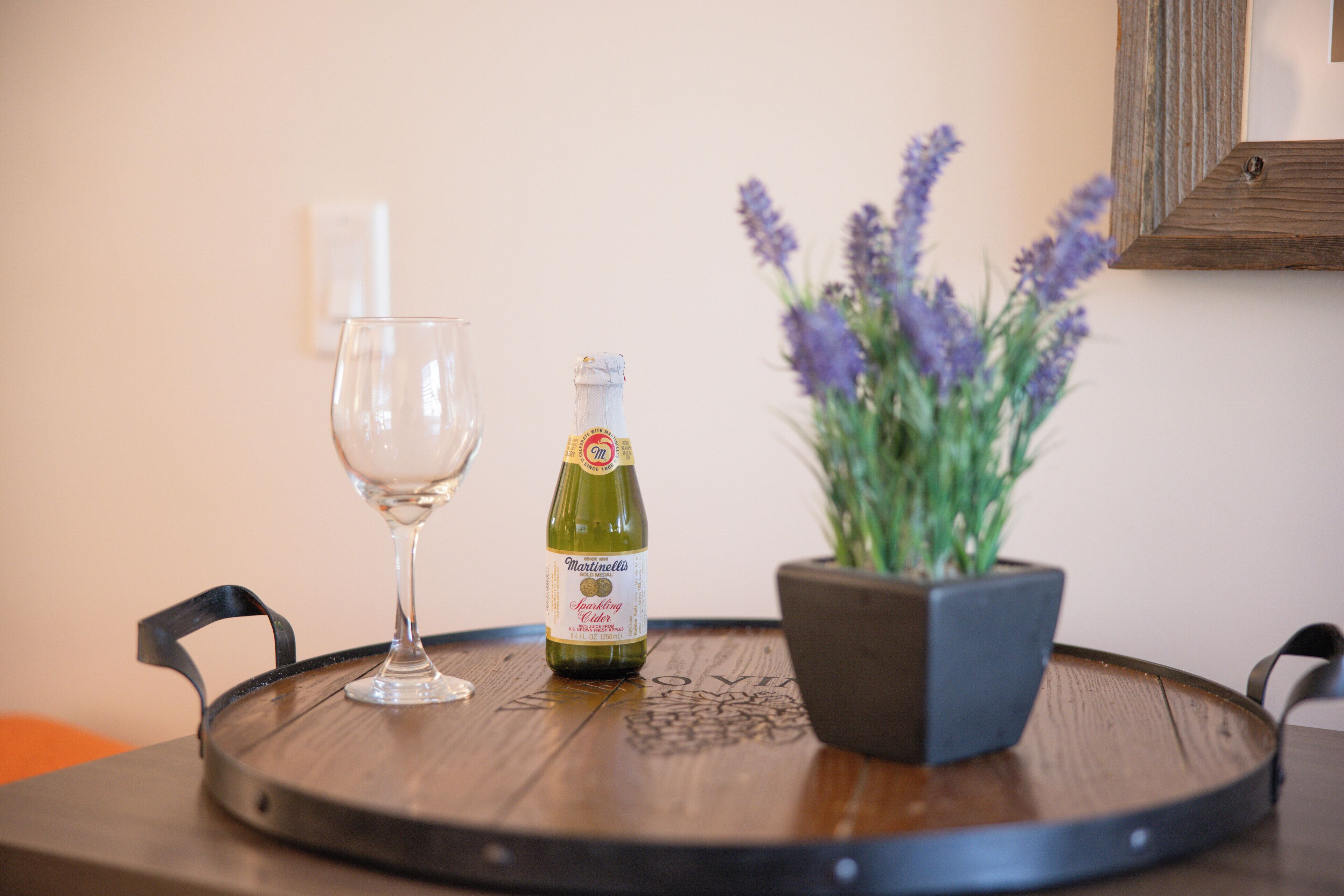 A round wooden table with a bottle of sparkling wine, a glass, and a potted lavender plant.