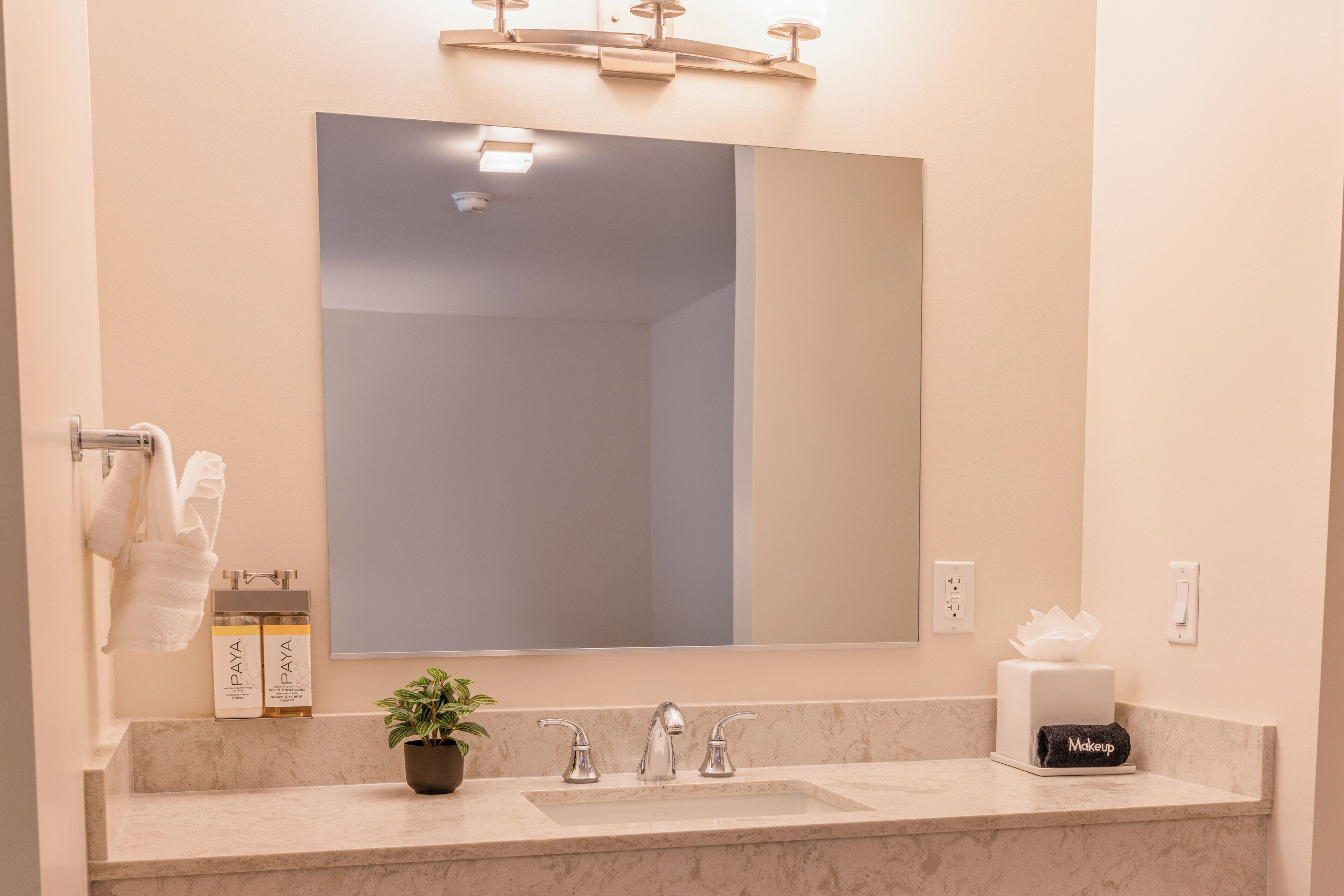 A bathroom with a large mirror, a sink, and a towel rack.