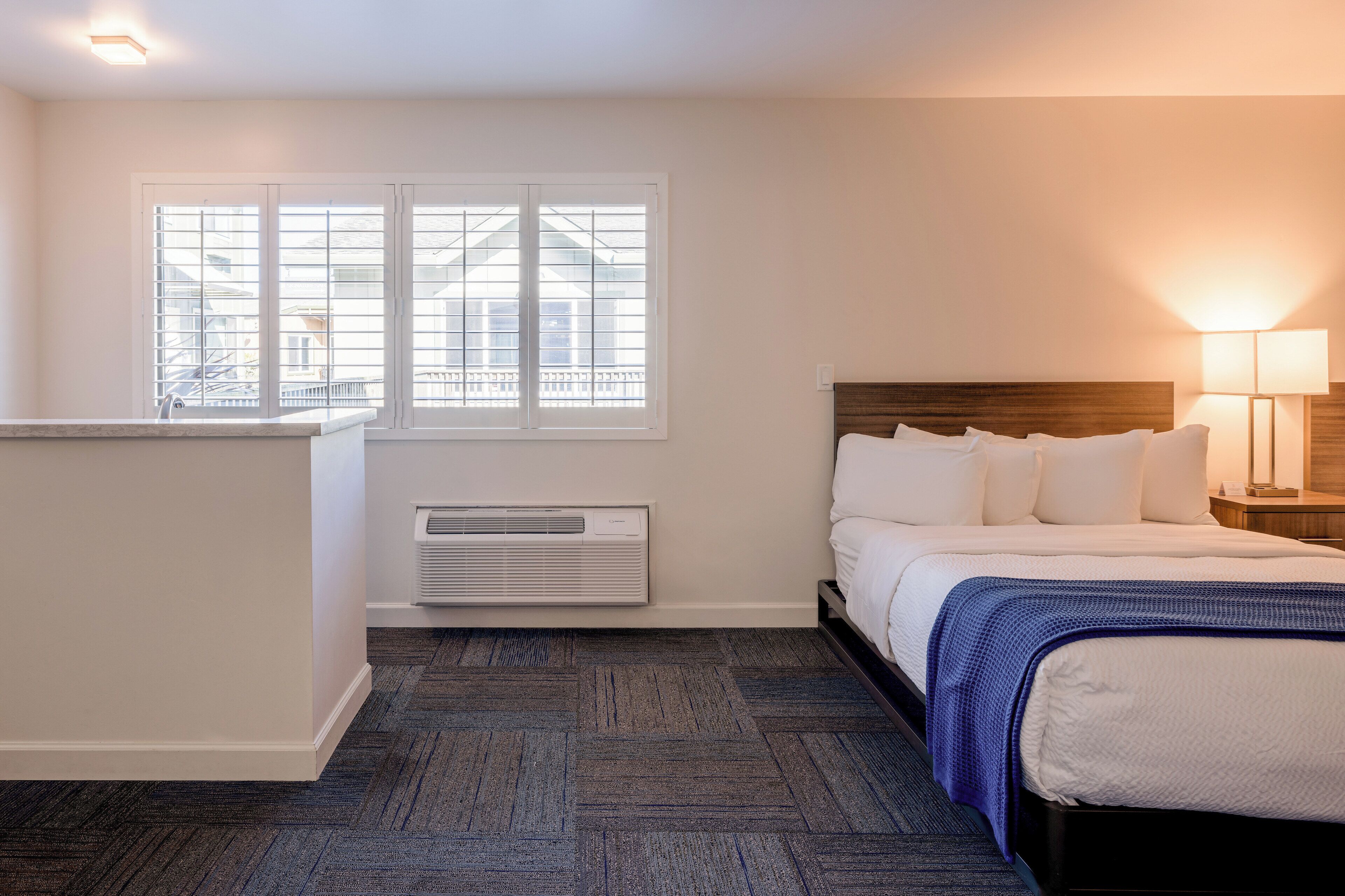 Een hotelkamer met een bed, nachtkastje, lamp, raam met zonwering en een radiator.