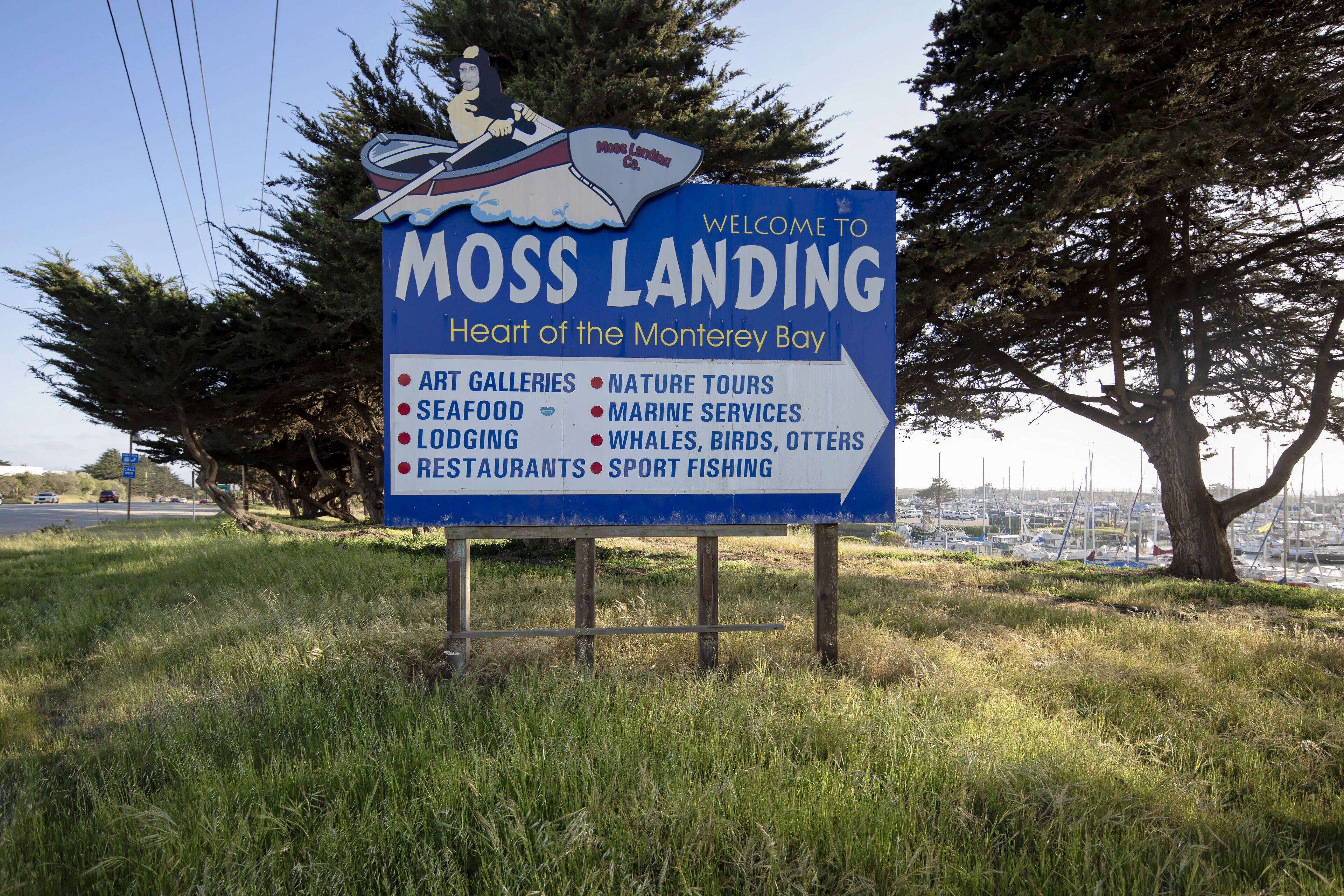 A welcome sign for Moss Landing, highlighting attractions like art galleries, seafood, lodging, and sport fishing.