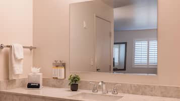 A bathroom with a marble countertop, a sink, a mirror, a towel rack, a potted plant, and a makeup dispenser.