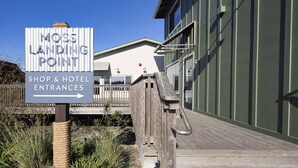 A wooden boardwalk leading to a building with a sign indicating 'Moss Landing Point' and 'Shop & Hotel Entrances'. - Inn At Moss Landing Point (Moss Landing)