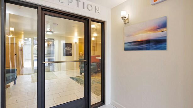 A reception area with a glass door, an exit sign, and a painting on the wall. - Inn At Moss Landing Point (Moss Landing)