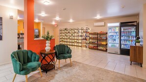 A modern lobby with green chairs, a coffee machine, a refrigerator stocked with beverages, and a wall with shelves of snacks. - Inn At Moss Landing Point (Moss Landing)