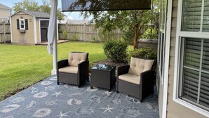 A covered patio area with two wicker chairs and a small table, a ceiling fan, and a view of the backyard. - Wilmington in the middle of it ALL (Wilmington)