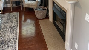 A living room with a fireplace, a television mounted above it, a striped armchair, a small table with decorative items, and a wicker basket. - Wilmington in the middle of it ALL (Wilmington)