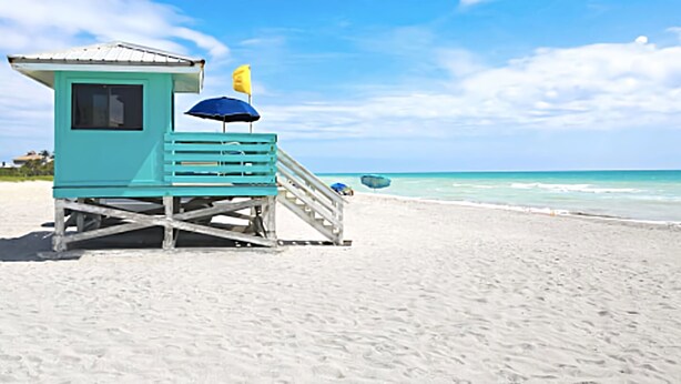 A lifeguard tower with a blue umbrella and a yellow flag on a sandy beach. - Close to Siesta Key  beach with a hot tub  and a large  garden (Sarasota)