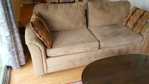 Een beige bank met gekleurde kussens, een houten vloer en een glazen tafel.