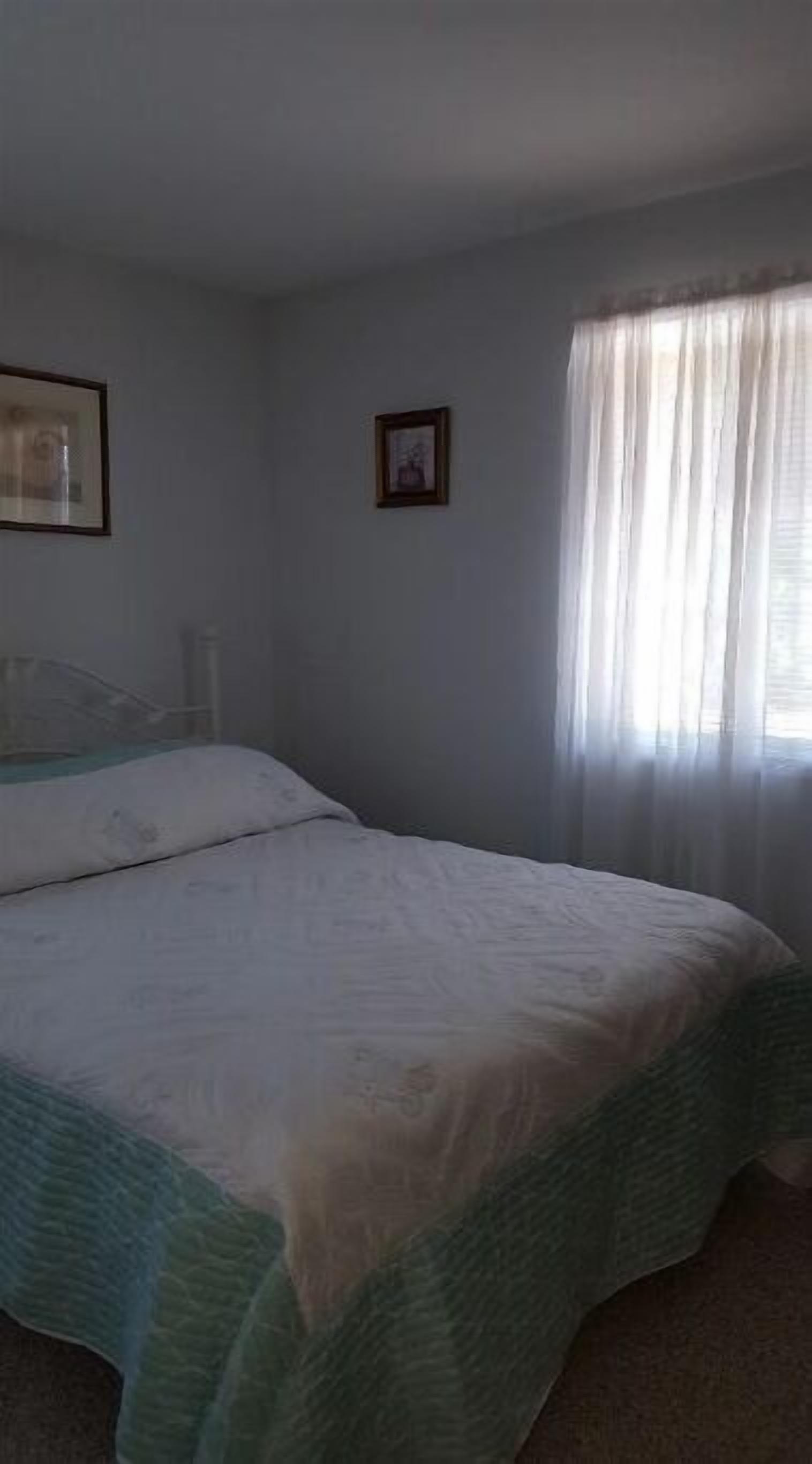 A bedroom with a bed, a window with curtains, and two framed pictures on the wall.