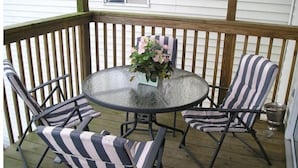 Een overdekt terras met een ronde glazen tafel, vier gestreepte stoelen en een plant in pot.