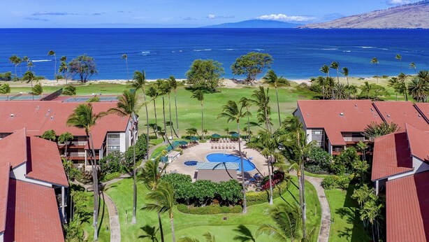 Ein Resort mit einem zentralen Pool, umgeben von Palmen und Blick auf den Ozean.