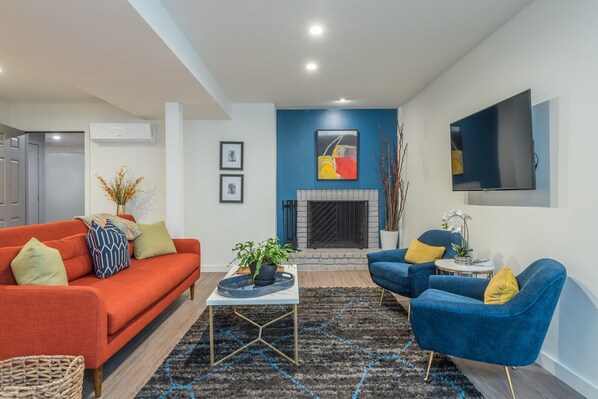 Una sala de estar moderna con un sofá rojo, sillones azules, una chimenea y un televisor de pantalla plana.