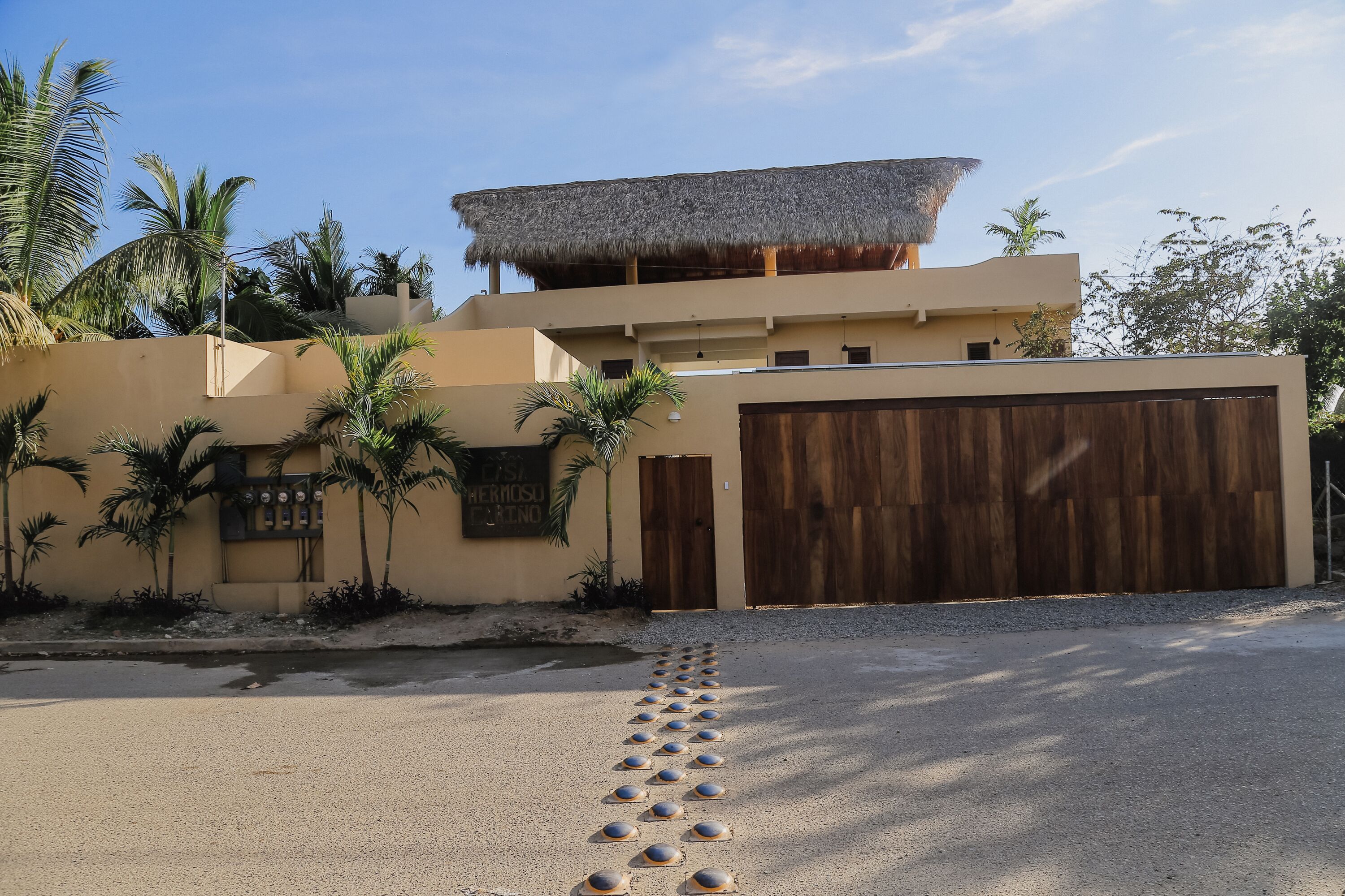 A modern building with a thatched roof, palm trees, and a large wooden garage door.