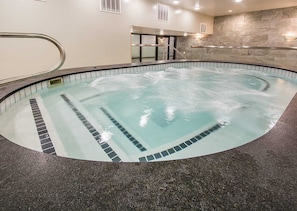 An indoor swimming pool with clear water, a tiled edge, and a stone wall in the background.