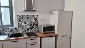Una cocina compacta con extractor de acero inoxidable, microondas y horno empotrado. Hay una ventana con vistas al exterior, y el suelo es de madera.