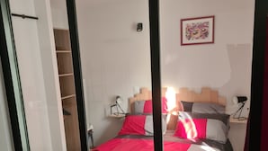 Un dormitorio con cama, dos lámparas de noche, cabecera de madera y colcha roja y blanca.