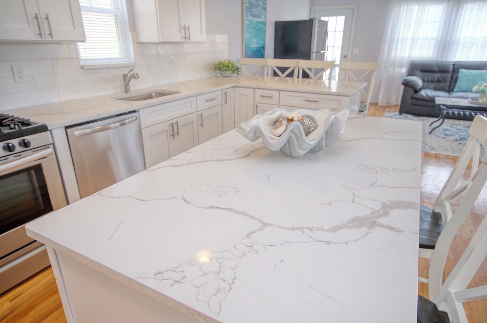 A modern kitchen with white cabinetry, a marble countertop, and a dining area with a white table and chairs.